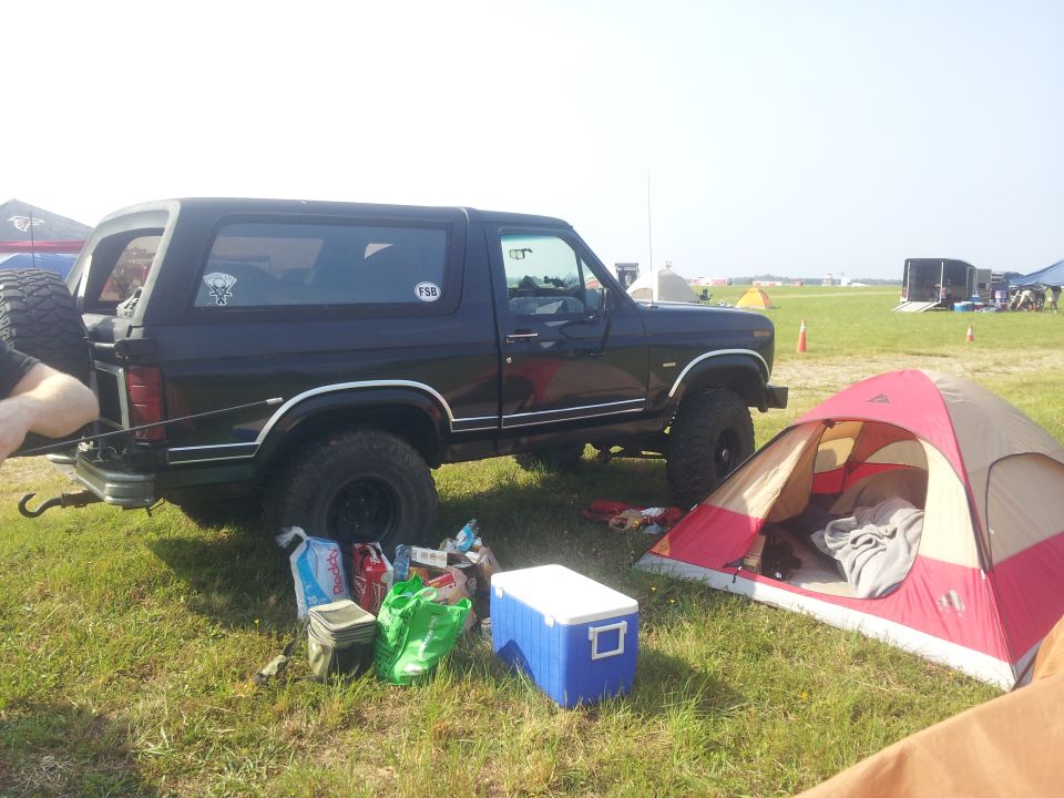 Black Ford Bronco parked in a grassy field next to a tent with camping gear.