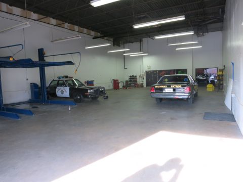 1991 Ford LTD Crown Victoria - Two black-and-white Highway Patrol sedans parked inside a garage, one beside a blue two-post lift.