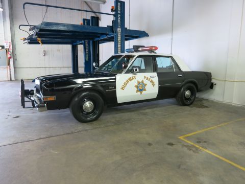 1991 Ford LTD Crown Victoria - Side view of a black-and-white Highway Patrol sedan with a front push bar and roof light bar parked in a garage.