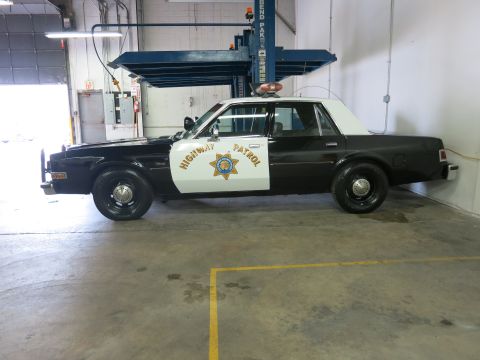 1991 Ford LTD Crown Victoria - Side profile of a black-and-white Highway Patrol sedan with door star emblem and roof light bar parked in a garage.