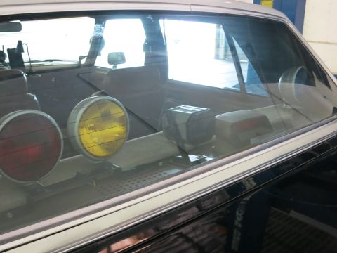 1991 Ford LTD Crown Victoria - Looking through a car's rear window at the interior, with red and amber auxiliary lamps and equipment mounted on the rear deck.