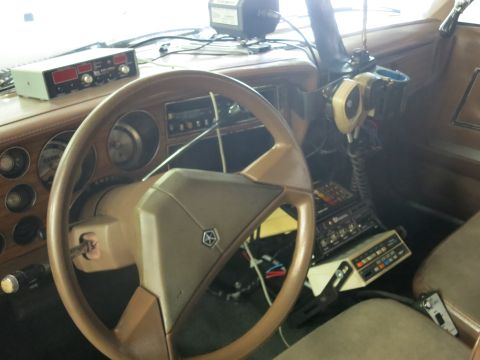 1991 Ford LTD Crown Victoria - tan car interior with a four-spoke steering wheel, dash-mounted two-way radios, a handheld microphone and a row of toggle switches.