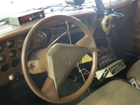 1991 Ford LTD Crown Victoria - Close interior view of a tan dashboard with a steering wheel bearing a pentastar emblem and several mounted radio and switch control panels.