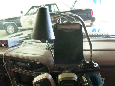 1991 Ford LTD Crown Victoria - gooseneck clipboard lamp mounted on a tan dashboard, with a black-and-white highway patrol car visible through the windshield.