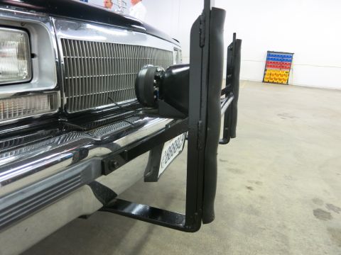 1991 Ford LTD Crown Victoria - black tubular push bumper carrying a small spotlight is bolted to the front of a dark car parked on a shop floor.