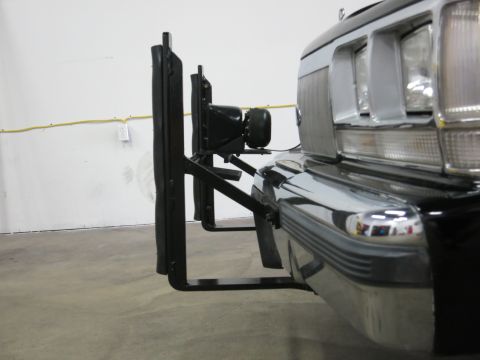 1991 Ford LTD Crown Victoria - Side view of a black tubular push bar with a mounted spotlight attached to the chrome bumper of a dark car on a shop floor.