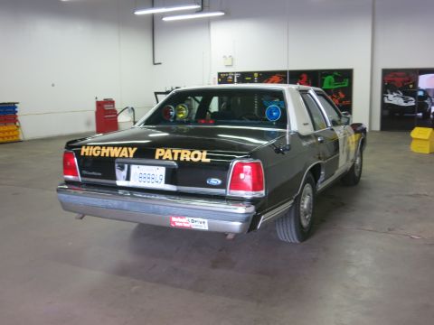 1991 Ford LTD Crown Victoria - Rear view of a dark Ford Crown Victoria sedan with HIGHWAY PATROL lettering and a Ford oval on the trunk, parked on a shop floor.