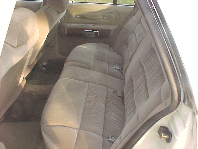 Back seat and door panel of a car interior. Tan fabric seats with horizontal pleats. Wood trim on door panel