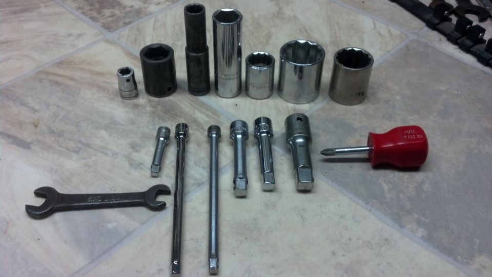 Assortment of sockets, extensions, and an open-end wrench arranged on tile