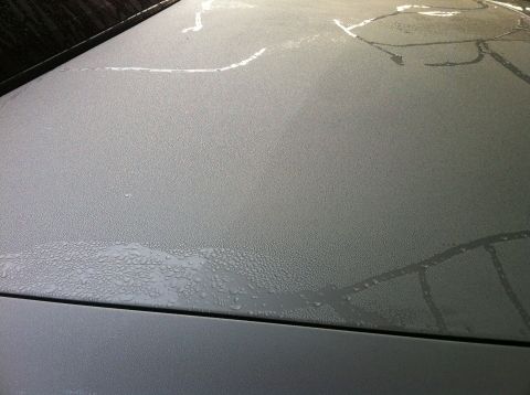 2003 Ford Crown Victoria - The textured surface of a vehicle's hood shows condensation droplets and streaks of water, suggesting it has been exposed to moisture.