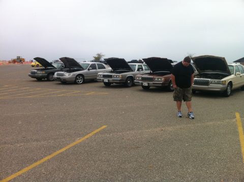 2003 Ford Crown Victoria - A man stands in a parking lot in front of a line of sedans with their hoods up. The cars appear to be older models, possibly from the 1990s…