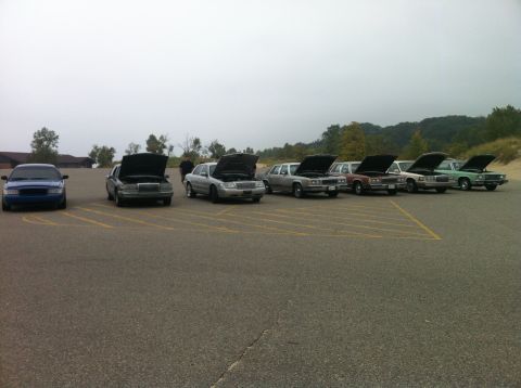 2003 Ford Crown Victoria - A line of sedans with hoods open are parked in a lot with yellow lines. A blue sedan is parked on the far left.