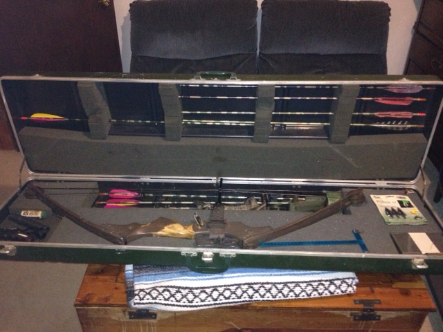 Open hard case with a camouflage compound bow and racked arrows on a wooden chest