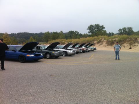 2003 Ford Crown Victoria - A line of Ford Crown Victoria sedans with hoods up are parked in a lot with a man standing to the right. A blue Crown Victoria is in the fo…