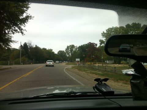 2003 Ford Crown Victoria - A view from inside a car shows a wet road ahead with trees on either side under an overcast sky.