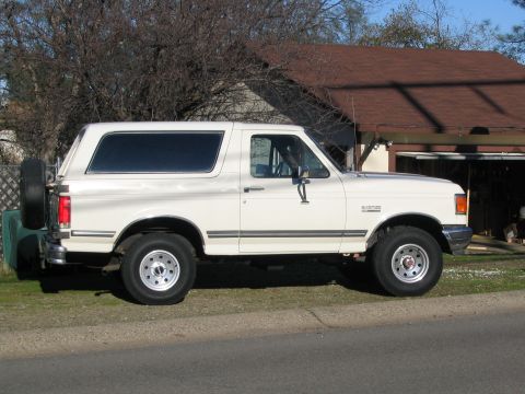 1989 Ford Bronco - This white 1989 Ford Bronco is shown from the side, its spare tire mounted on the rear door.