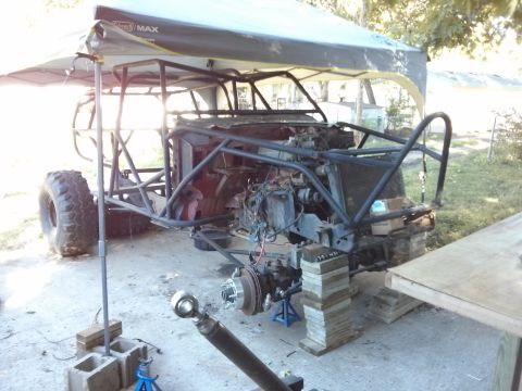 1986 Ford Bronco - A custom-built off-road buggy with a roll cage is under construction outdoors, supported by blocks and jack stands. A large tire is visible…