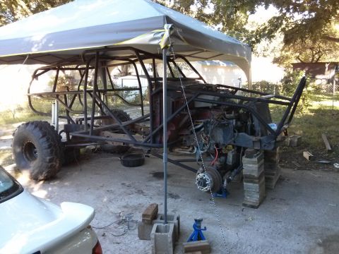 1986 Ford Bronco - A custom-built off-road vehicle chassis is under construction, supported by cinder blocks and wooden planks. The vehicle is partially cover…