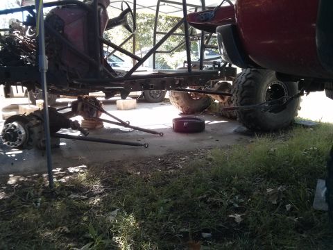 1986 Ford Bronco - The chassis and drivetrain of a custom off-road vehicle are shown disassembled, with the front axle and suspension components laid out on t…