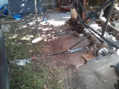 1986 Ford Bronco - A partially disassembled vehicle chassis with the rear axle and suspension components visible, resting on wooden blocks on a concrete surfa…