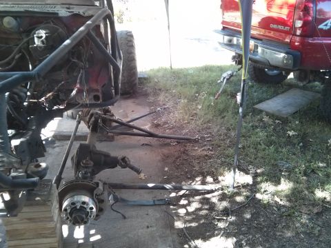 1986 Ford Bronco - A heavily modified off-road vehicle, likely a Ford Bronco, is undergoing repairs or modifications outdoors. The front axle and suspension c…