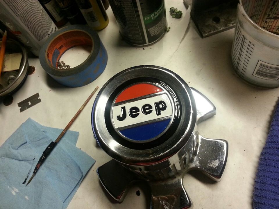 Chrome Jeep emblem with red, white, and blue coloring on a workbench with repair tools.