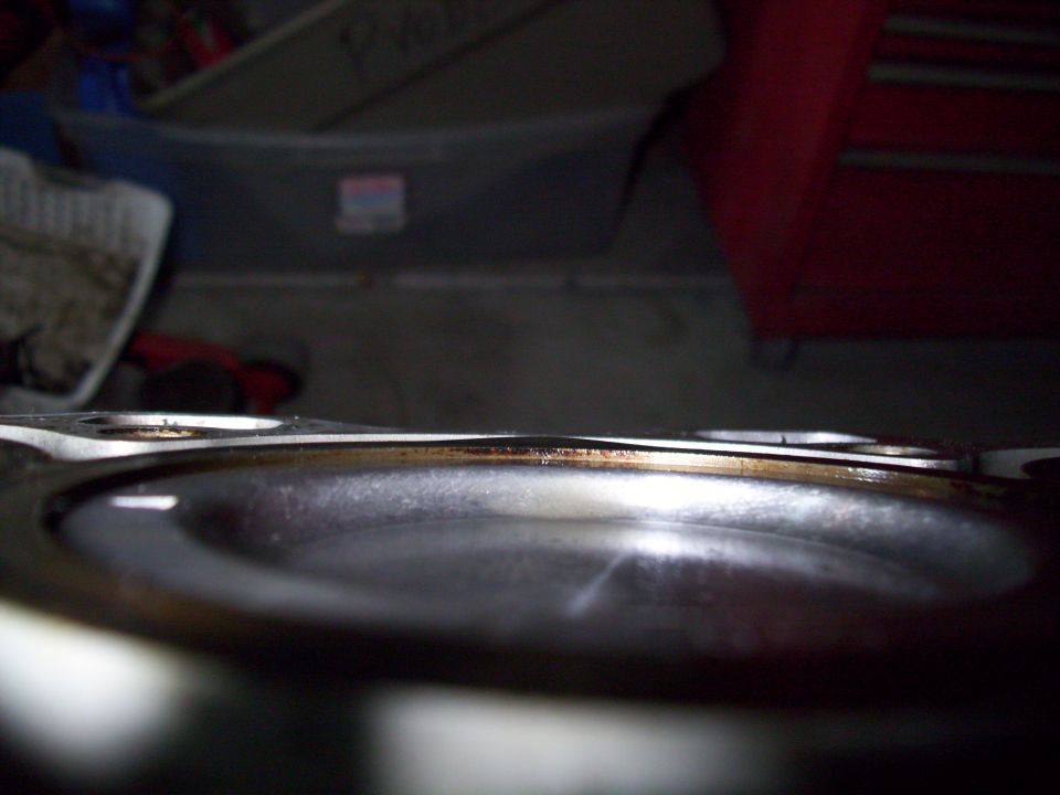 Close-up of a worn metal engine gasket with a dark recess and discolored edge.