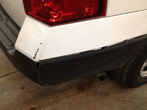 1991 Ford LTD Crown Victoria - Photograph of a white SUV's rear bumper showing minor damage and a loose lower trim panel, not a technical document.