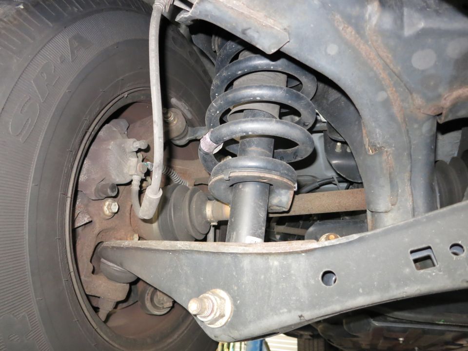 Photo of front suspension with coil spring, shock and control arm behind a tire