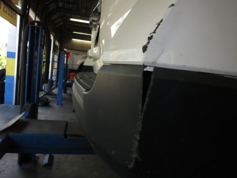 1991 Ford LTD Crown Victoria - Photograph of a white vehicle's cracked rear bumper corner in a service bay, not a technical document.