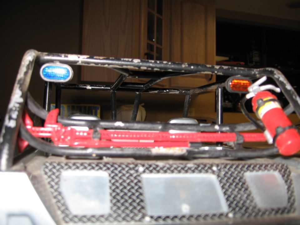 Rear view of a modified off-road vehicle with a roll cage, jack, and fire extinguisher.