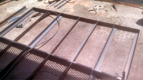 1979 Ford Bronco - A metal frame is being constructed on a concrete surface. Tools such as a welding torch, clamps, and a level are visible nearby.