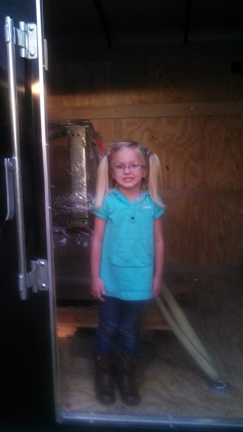 1979 Ford Bronco - A young girl with blonde pigtails and glasses stands inside what appears to be a trailer or cargo area.