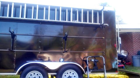 1979 Ford Bronco - The side of a dark-colored utility trailer is shown, equipped with a ladder rack on top and horizontal bars mounted to the side. A cordless…