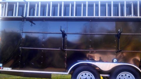 1979 Ford Bronco - Side view of a black trailer with a silver ladder rack mounted on top. The trailer has two axles with silver fenders and visible tires.