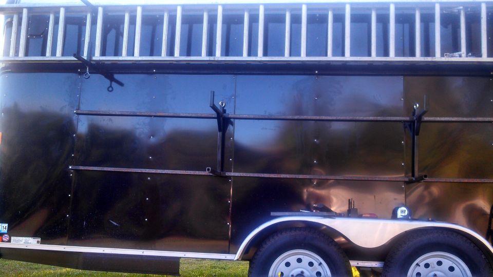 Side view of a black trailer with a ladder rack and dual axles.