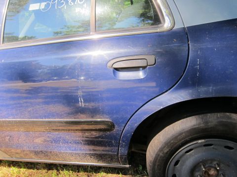 2001 Ford Crown Victoria - Close-up side view of a blue sedan showing the rear door handle, a portion of the rear wheel well, and a black trim piece along the lower d…