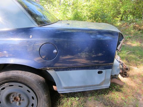 2001 Ford Crown Victoria - The rear quarter panel and wheel well of a dark blue sedan are visible. The car appears to be in a state of disrepair, with visible rust an…