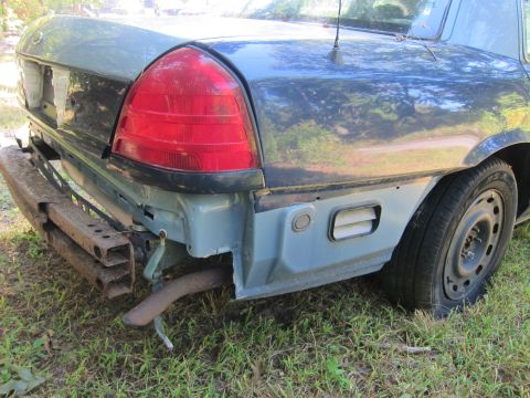 2001 Ford Crown Victoria - The rear passenger side of a dark blue Ford Crown Victoria is shown with the bumper removed, revealing the exhaust pipe and rusted frame co…