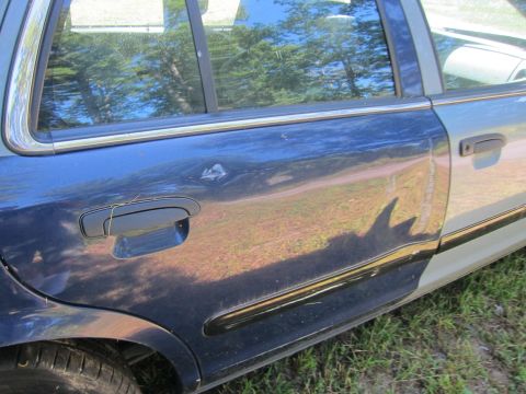 2001 Ford Crown Victoria - The side of a blue and silver sedan shows a dent on the rear passenger door and a scratch near the front passenger door handle. The car is…