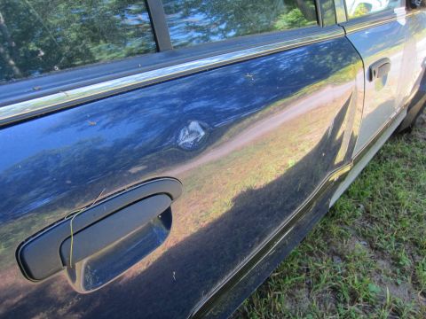 2001 Ford Crown Victoria - A close-up view of the driver's side door of a dark blue sedan, showing a dent near the door handle and a dent on the rear door. The car is…