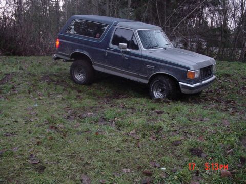 1987 Ford Bronco - A 1987 Ford Bronco is shown from a three-quarter front angle, parked on uneven terrain.