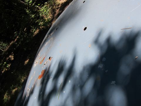 2001 Ford Crown Victoria - A close-up, angled view of a light blue car hood shows rust spots and shadows from foliage. Several small holes are visible on the surface.