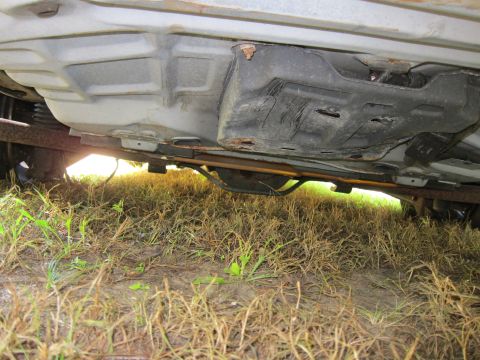 2001 Ford Crown Victoria - The underside of a vehicle, likely a 2001 Ford Crown Victoria, showing the fuel tank and exhaust system. The vehicle is parked on a grassy…