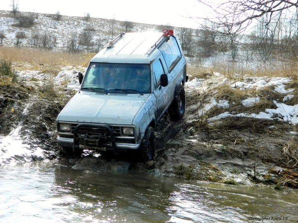 Light-colored SUV driving through a muddy stream, off-road.
