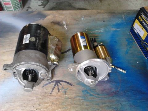 1979 Ford Ranchero - Side-by-side comparison on a paint-stained workbench of a large old black cast-iron starter motor and a smaller new gear-reduction mini sta…