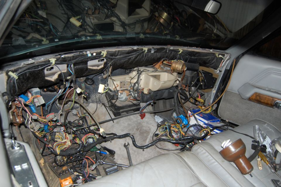 Disassembled dashboard of a car with exposed wiring and components, gray leather seats visible