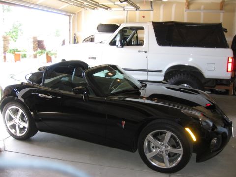 1995 Ford Bronco - A black convertible is parked in front of a white SUV inside a garage.