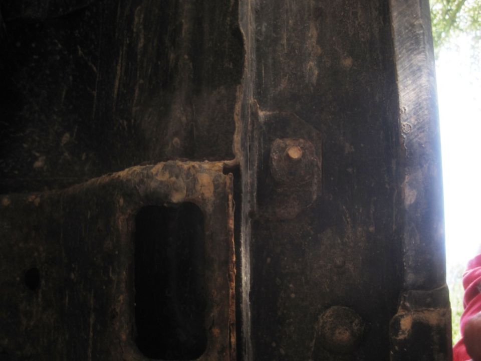 Close-up of heavily rusted, dark metal frame section with bolt holes