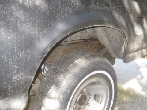 1993 Ford Bronco - Close-up of the rear wheel well and tire of a black vehicle, showing rust and wear.